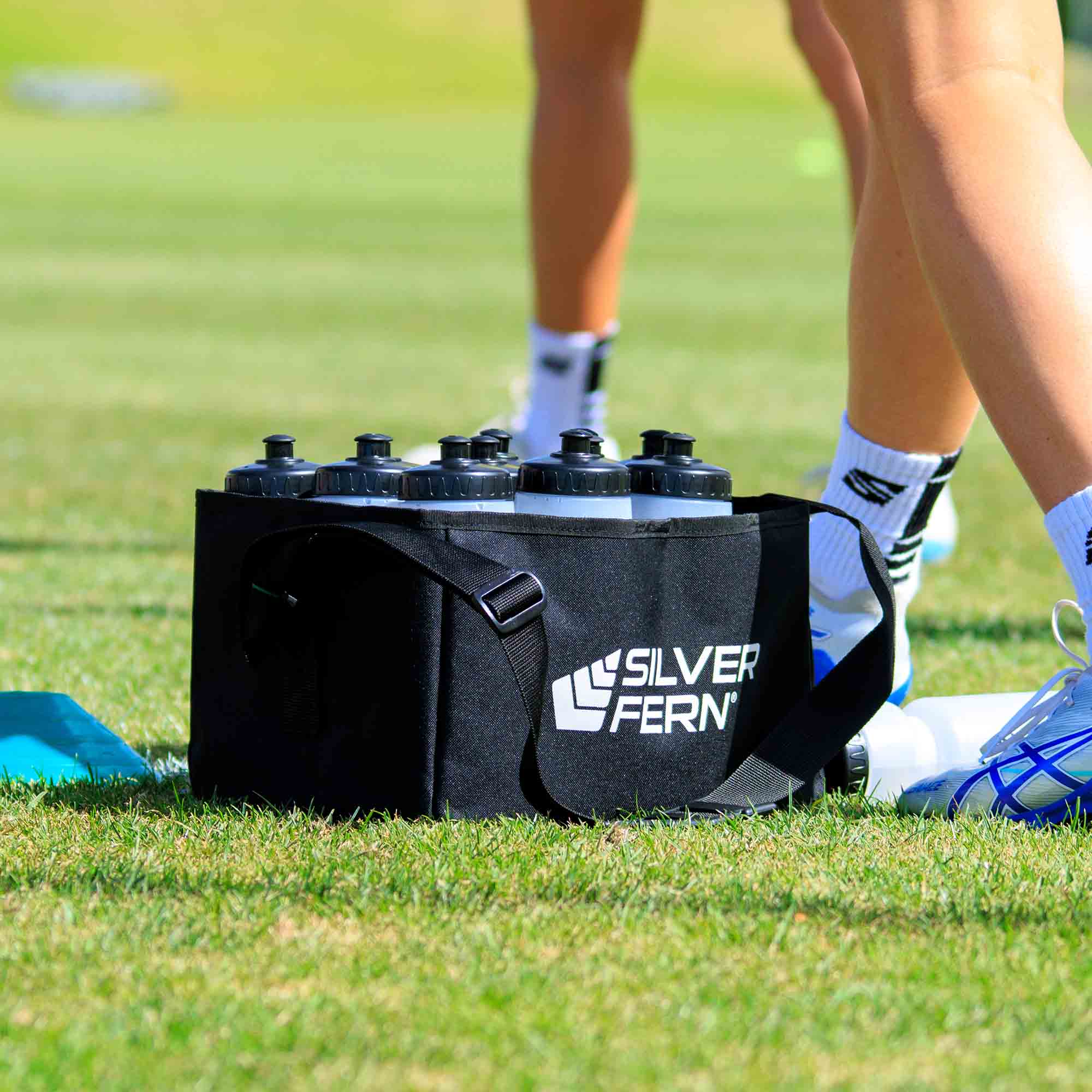 Drink bottle carrier fabric, 12 bottles capacity, bottle in drink carrier on field, lifestyle.