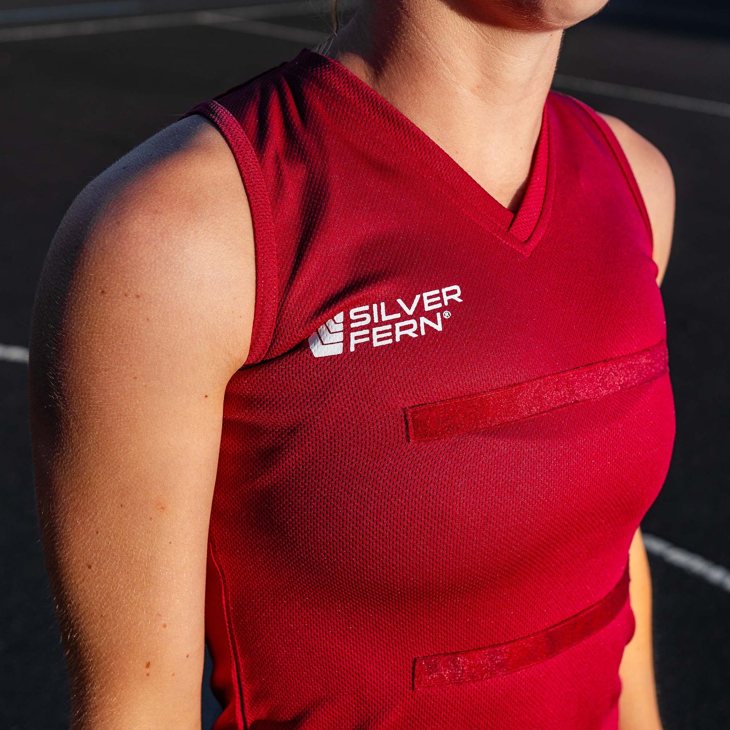 Close-up of a netball player wearing a maroon dress uniform, focusing on the upper body and the Silver Fern logo on the chest.