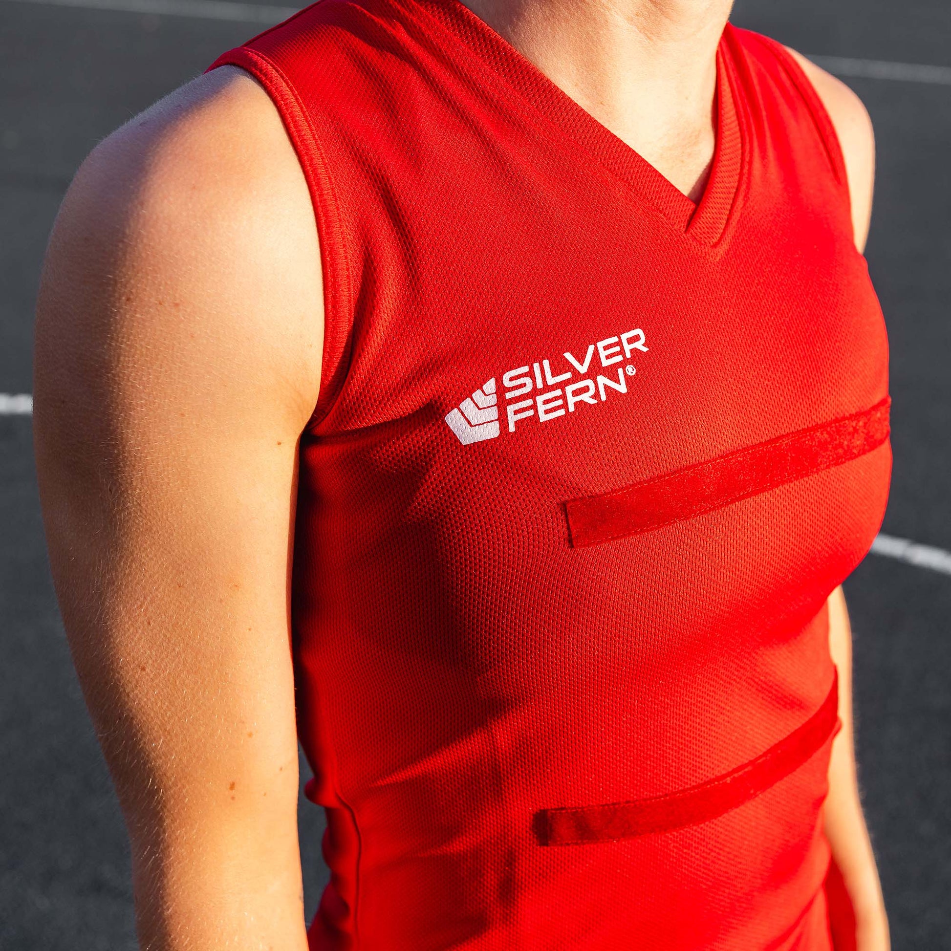 Close-up of a netball player wearing a red dress uniform, focusing on the upper body and the Silver Fern logo on the chest.