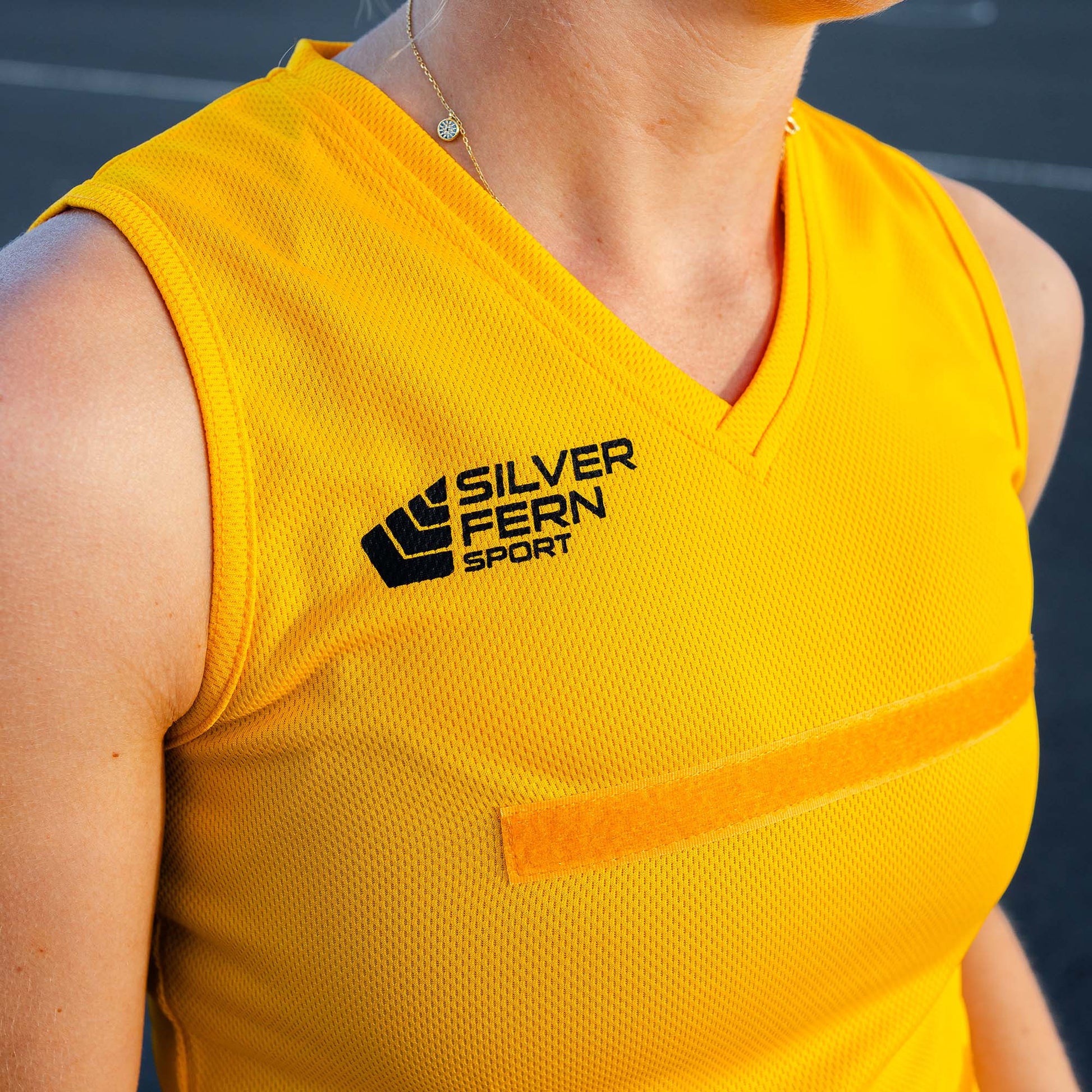 Close-up of a netball player wearing a yellow dress uniform, focusing on the upper body and the Silver Fern logo on the chest.