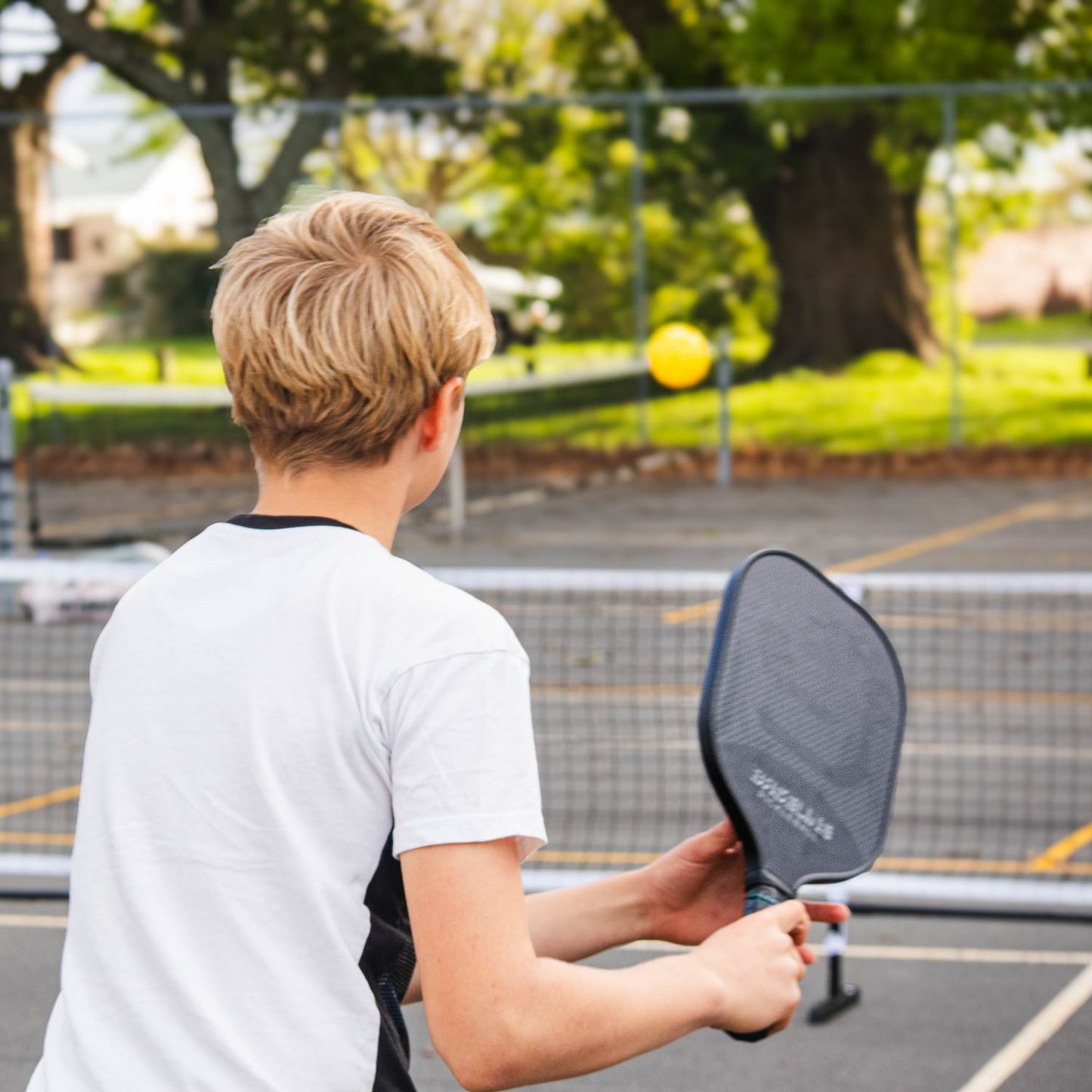 Pickleball Full Size Net Set, Action shot, kid holding a paddle preparing the swing to hit the pickleball