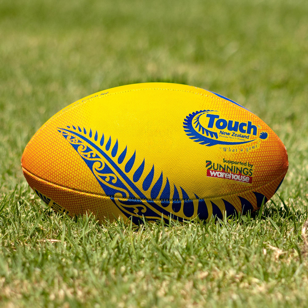 Silver Fern Touch Rugby Ball Amber Blaze Trainer, Lifestyle shot, sitting on a rugby field