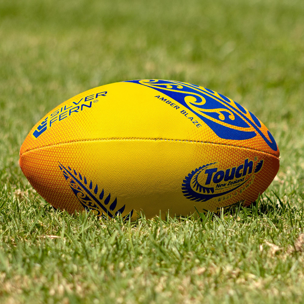Silver Fern Touch Rugby Ball Amber Blaze Trainer, Lifestyle shot, sitting on a rugby field
